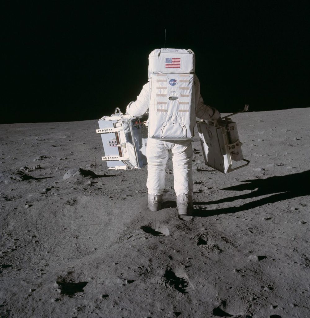 Astronaut Edwin E. Aldrin Jr., lunar module pilot, deploys two components of the Early Apollo Scientific Experiments Package on the surface of the Moon during the Apollo 11 extravehicular activity in 1969. A seismic experiment is in his left hand, and in his right is a laser-reflecting panel. Astronaut Neil A. Armstrong, mission commander, took this photograph.